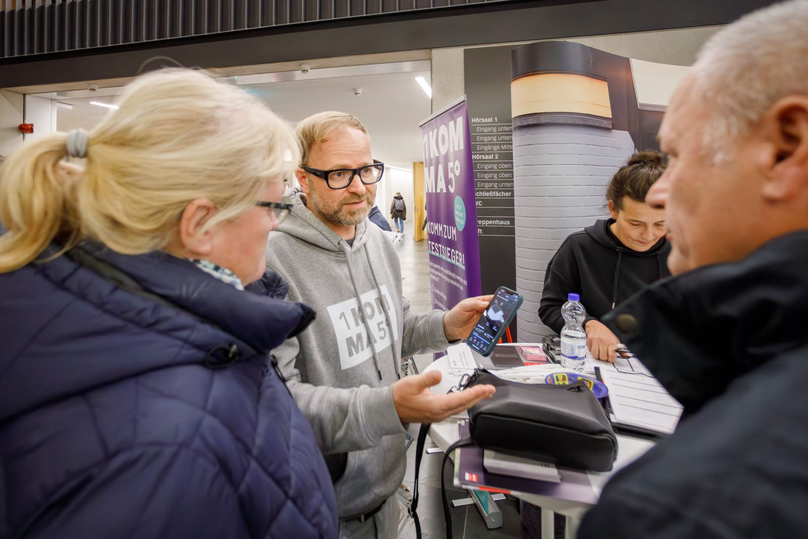 Berater zeigt Besucher:innen eine App auf dem Smartphone am Stand beim Wärmepumpen-Infotag in Erfurt