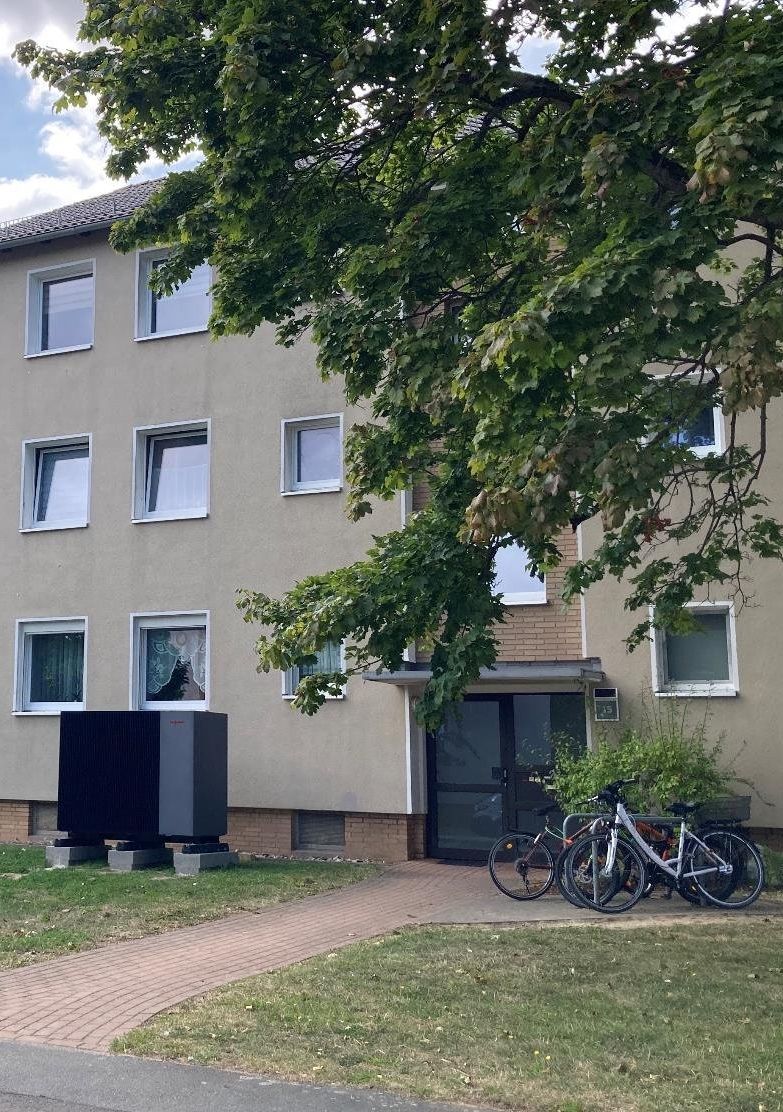 Mehrfamilienhaus aus den 60er-Jahren mit großer Wärmepumpe vor dem Eingang