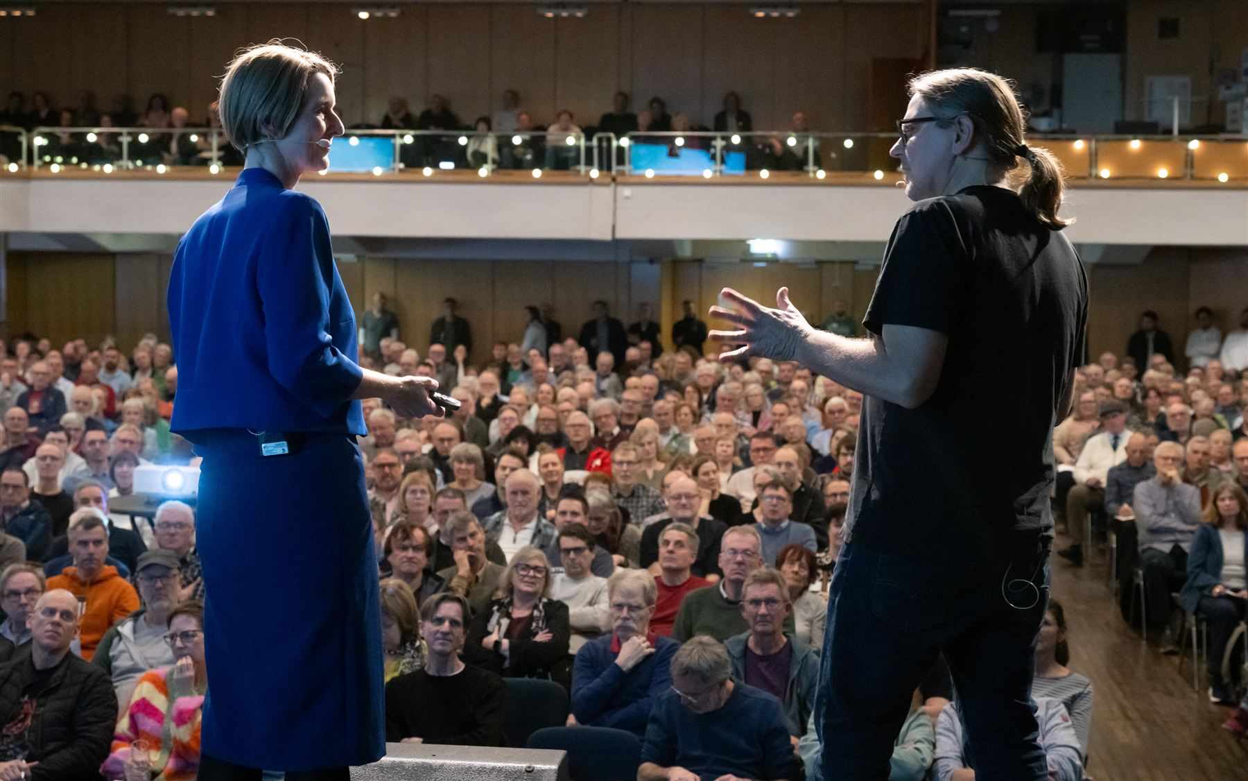 Anja Floetenmeyer-Woltmann und Carsten Herbert von hinten auf der Bühne in Bonn, Blick ins Publikum